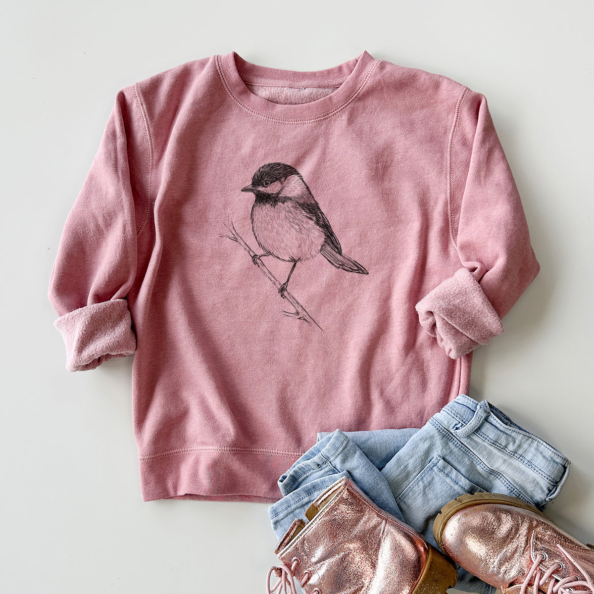 Youth crewneck sweatshirt printed with a detailed black ink sketch of a black-capped chickadee perched on a branch, styled flat with jeans and boots.