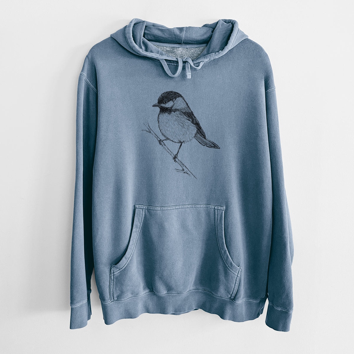 Slate blue pigment dyed hoodie laid flat, printed with a detailed black ink sketch of a black-capped chickadee perched on a branch.
