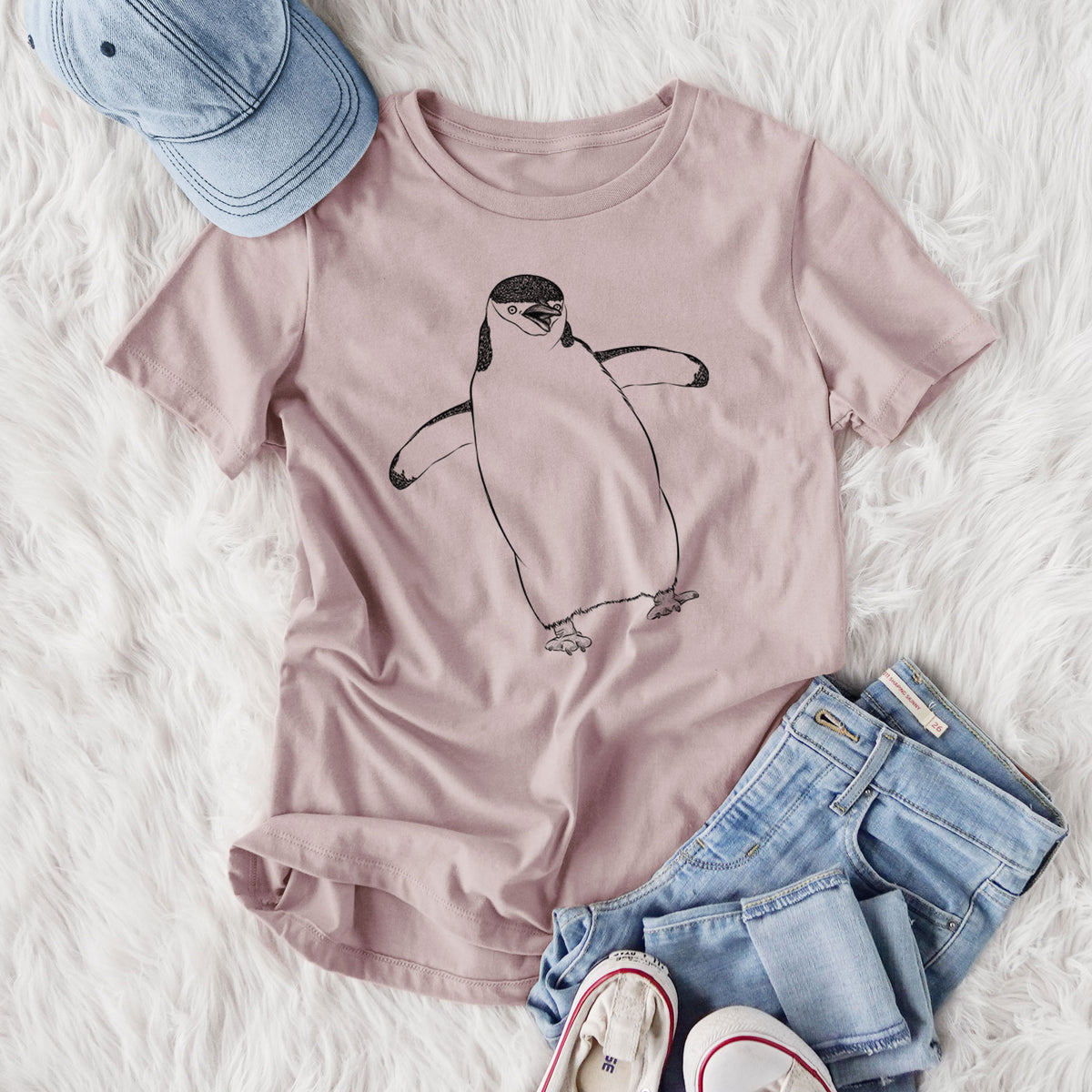 Women's relaxed fit cotton t-shirt printed with a black ink illustration of a chinstrap penguin standing with its flippers out, styled flat on a white faux fur rug with jeans.