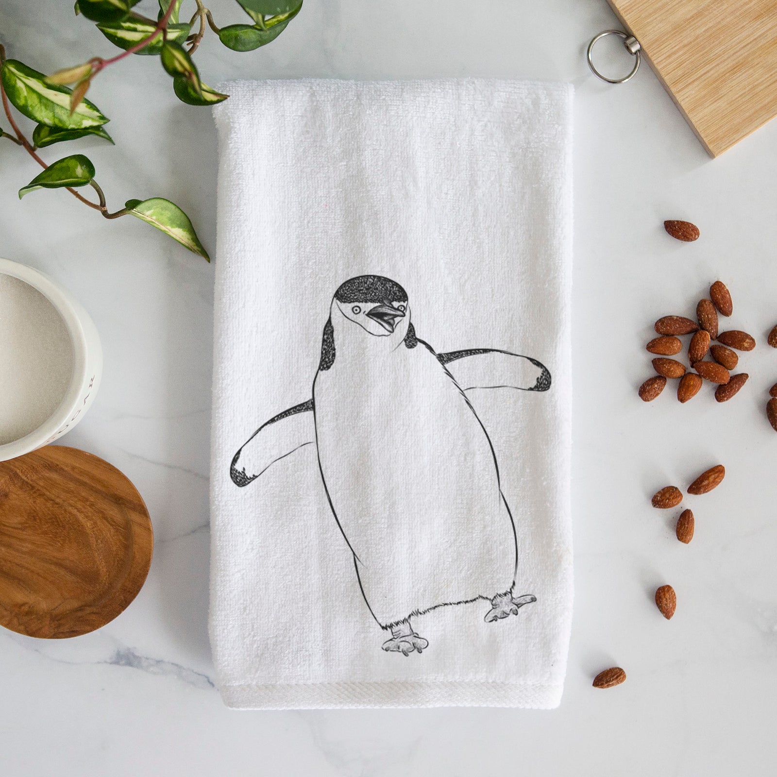 White hand towel printed with a black ink illustration of a chinstrap penguin standing with its flippers out.