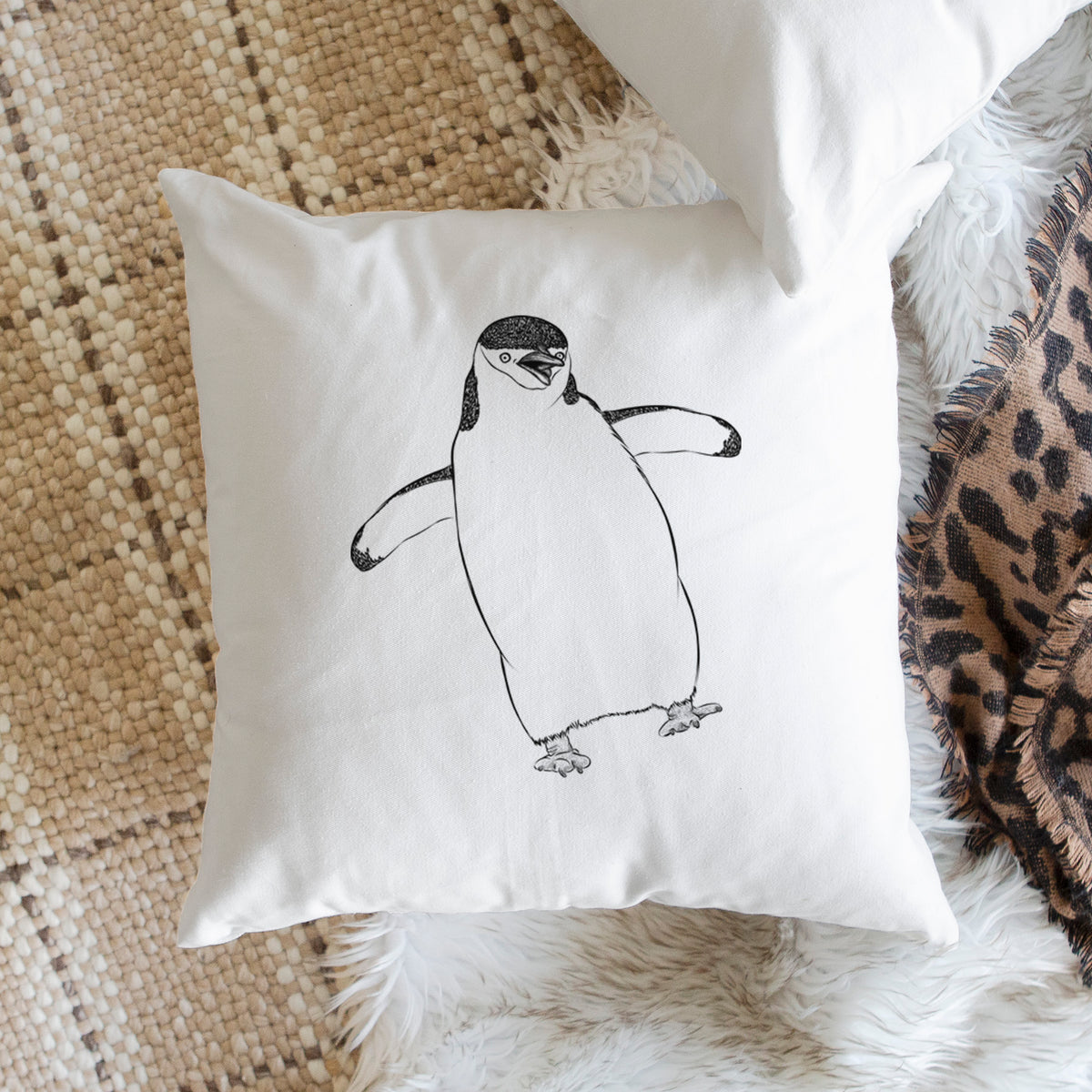 White pillow cover printed with a black ink illustration of a chinstrap penguin standing with its flippers out, on a woven chair.