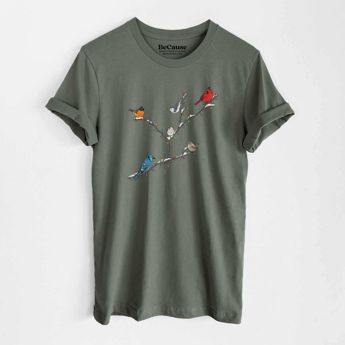 Military green lightweight cotton t-shirt laid flat, printed with a full-color illustration of winter backyard birds, including a cardinal, blue jay and robin, perched on bare branches.