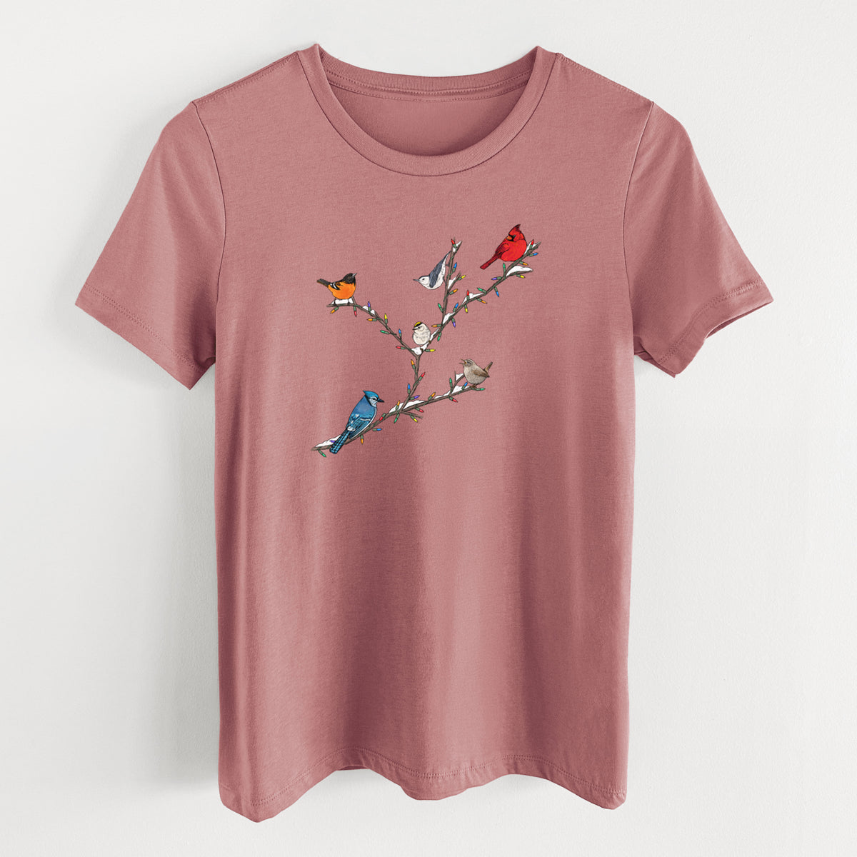 Mauve pink women's relaxed fit cotton t-shirt laid flat, printed with a full-color illustration of winter backyard birds, including a cardinal, blue jay and robin, perched on bare branches.