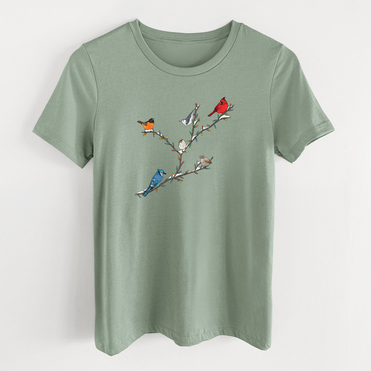 Sage green women's relaxed fit cotton t-shirt laid flat, printed with a full-color illustration of winter backyard birds, including a cardinal, blue jay and robin, perched on bare branches.
