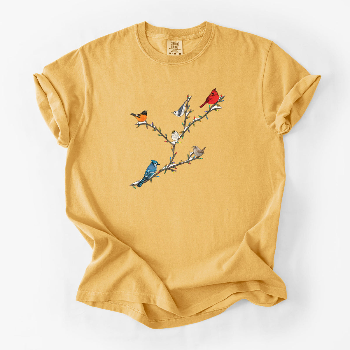Golden wheat yellow Comfort Colors t-shirt laid flat, printed with a full-color illustration of winter backyard birds, including a cardinal, blue jay and robin, perched on bare branches.