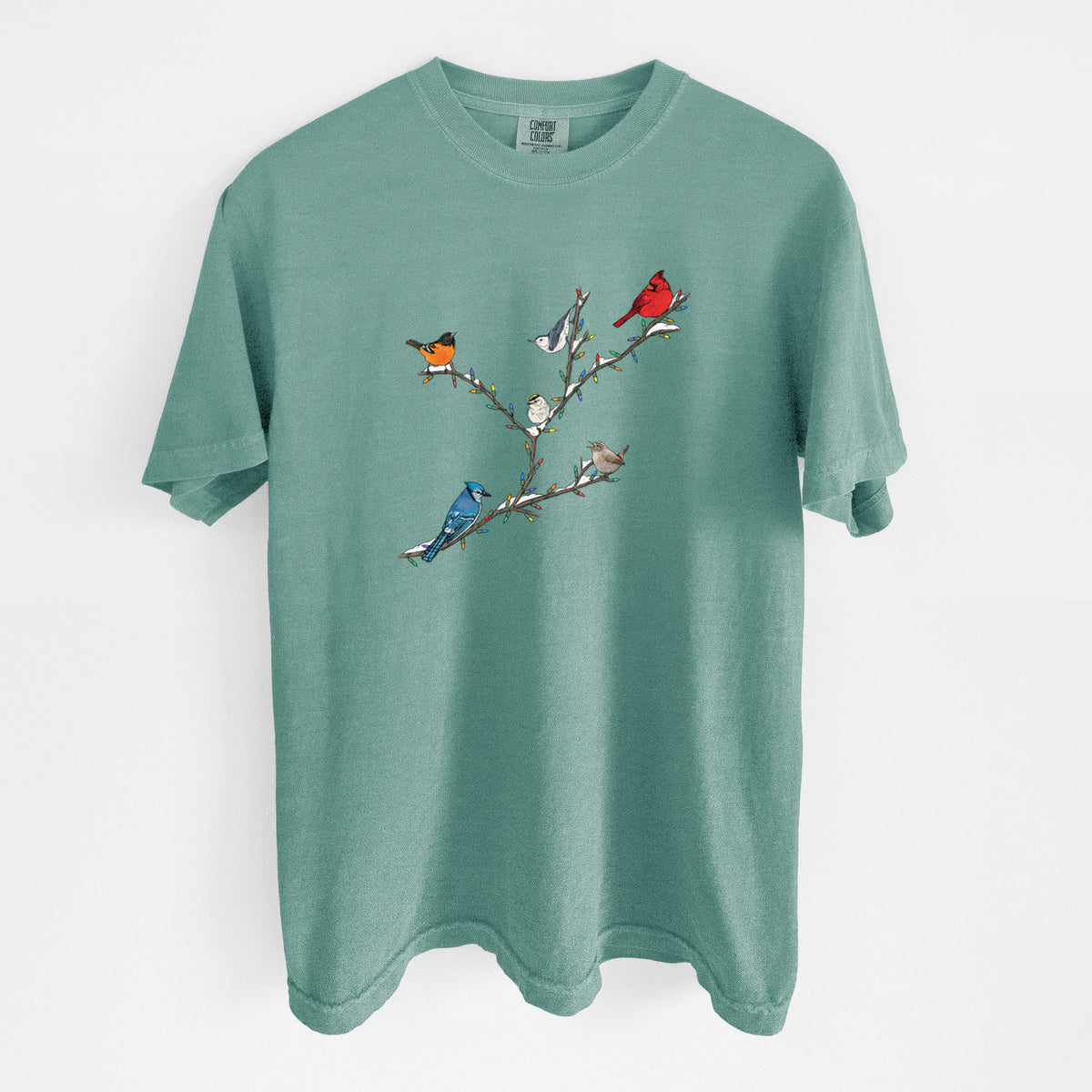 Reef green Comfort Colors t-shirt laid flat, printed with a full-color illustration of winter backyard birds, including a cardinal, blue jay and robin, perched on bare branches.