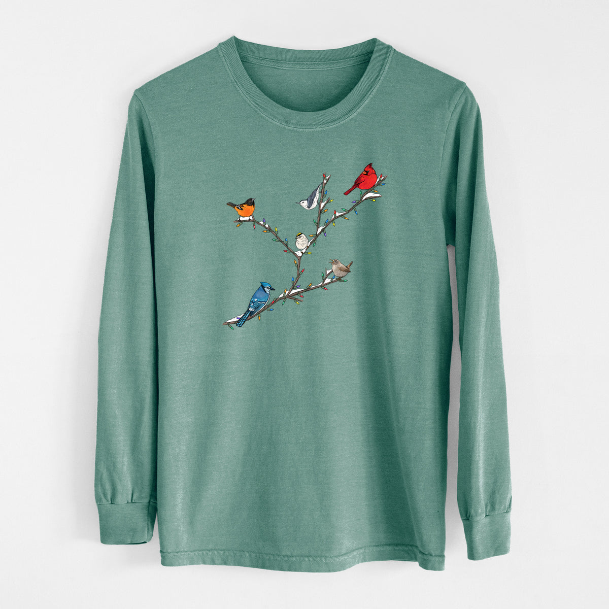 Pine green Comfort Colors long sleeve shirt laid flat, printed with a full-color illustration of winter backyard birds, including a cardinal, blue jay and robin, perched on bare branches.