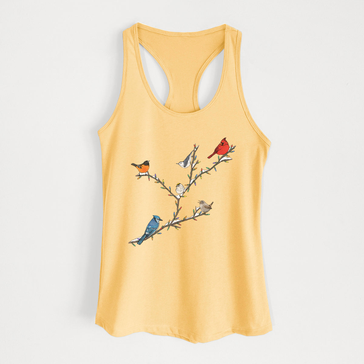 Banana cream women's racerback tank top laid flat, printed with a full-color illustration of winter backyard birds, including a cardinal, blue jay and robin, perched on bare branches.