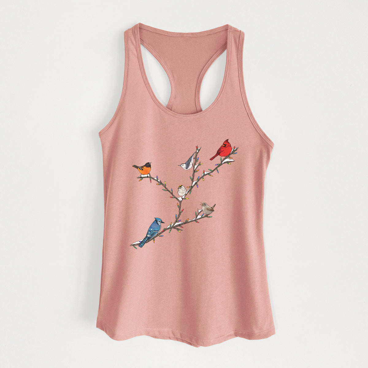 Desert pink women's racerback tank top laid flat, printed with a full-color illustration of winter backyard birds, including a cardinal, blue jay and robin, perched on bare branches.