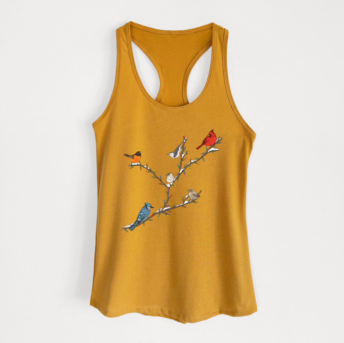 Gold women's racerback tank top laid flat, printed with a full-color illustration of winter backyard birds, including a cardinal, blue jay and robin, perched on bare branches.