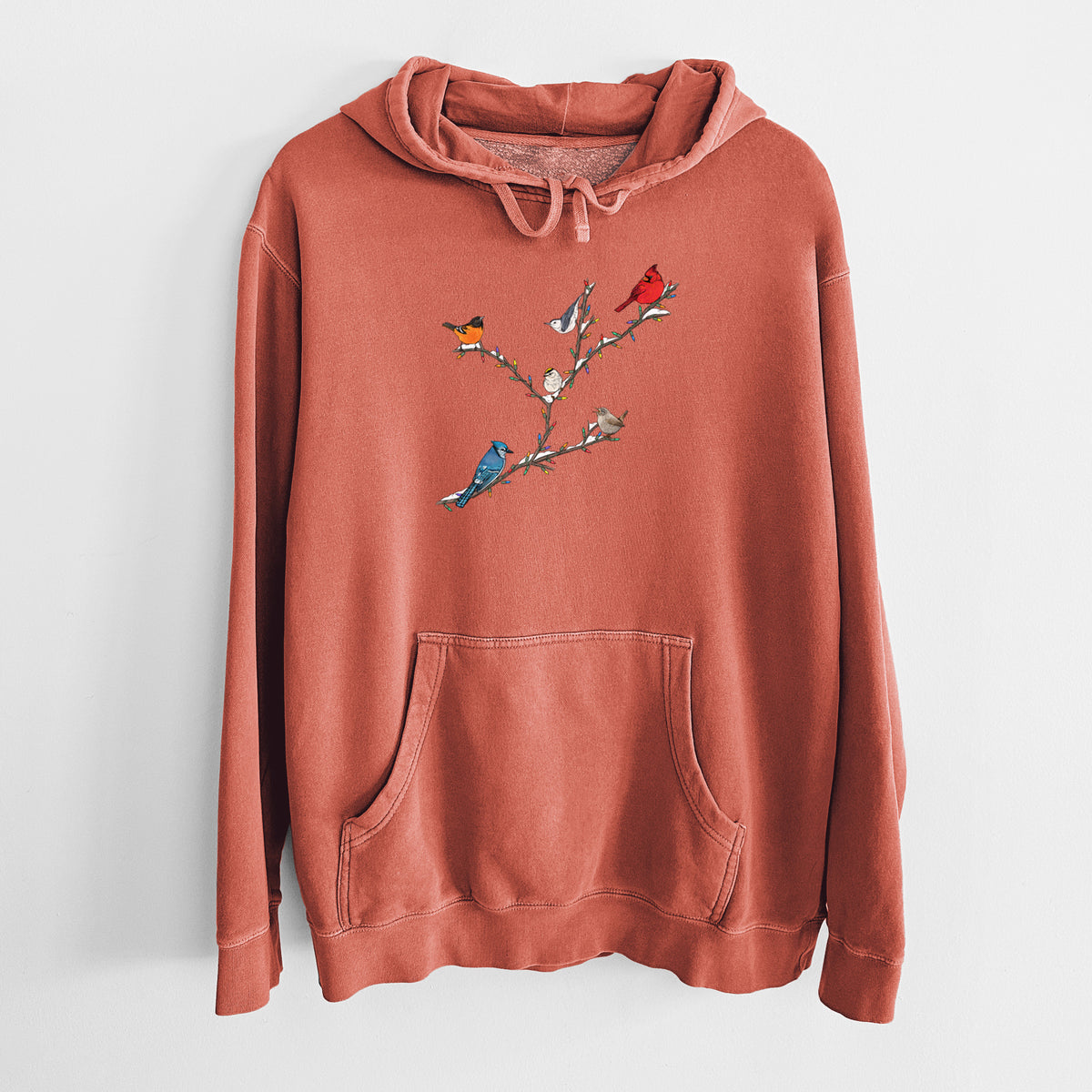 Amber orange pigment dyed hoodie laid flat, printed with a full-color illustration of winter backyard birds, including a cardinal, blue jay and robin, perched on bare branches.