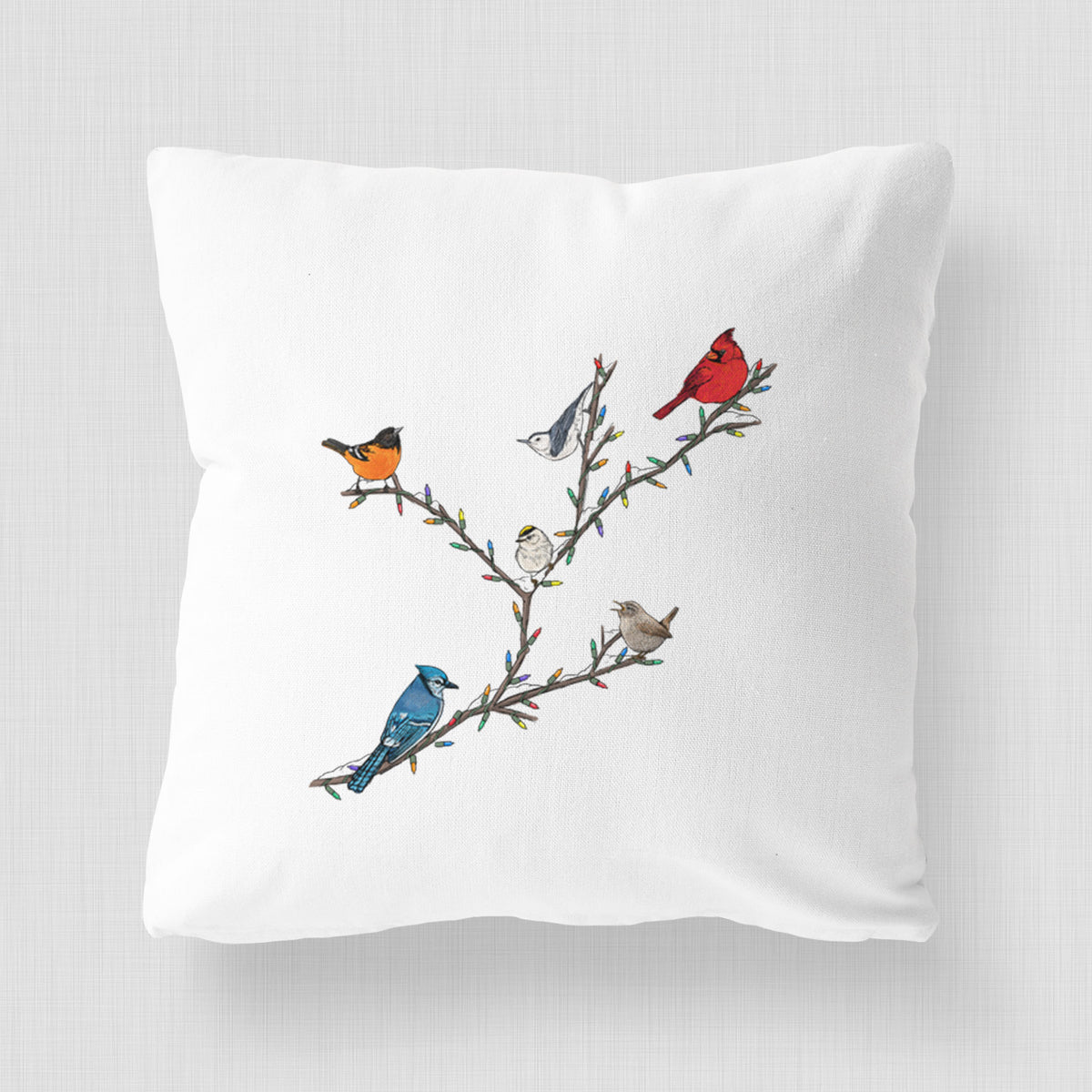 White pillow cover printed with a full-color illustration of winter backyard birds, including a cardinal, blue jay and robin, perched on bare branches.