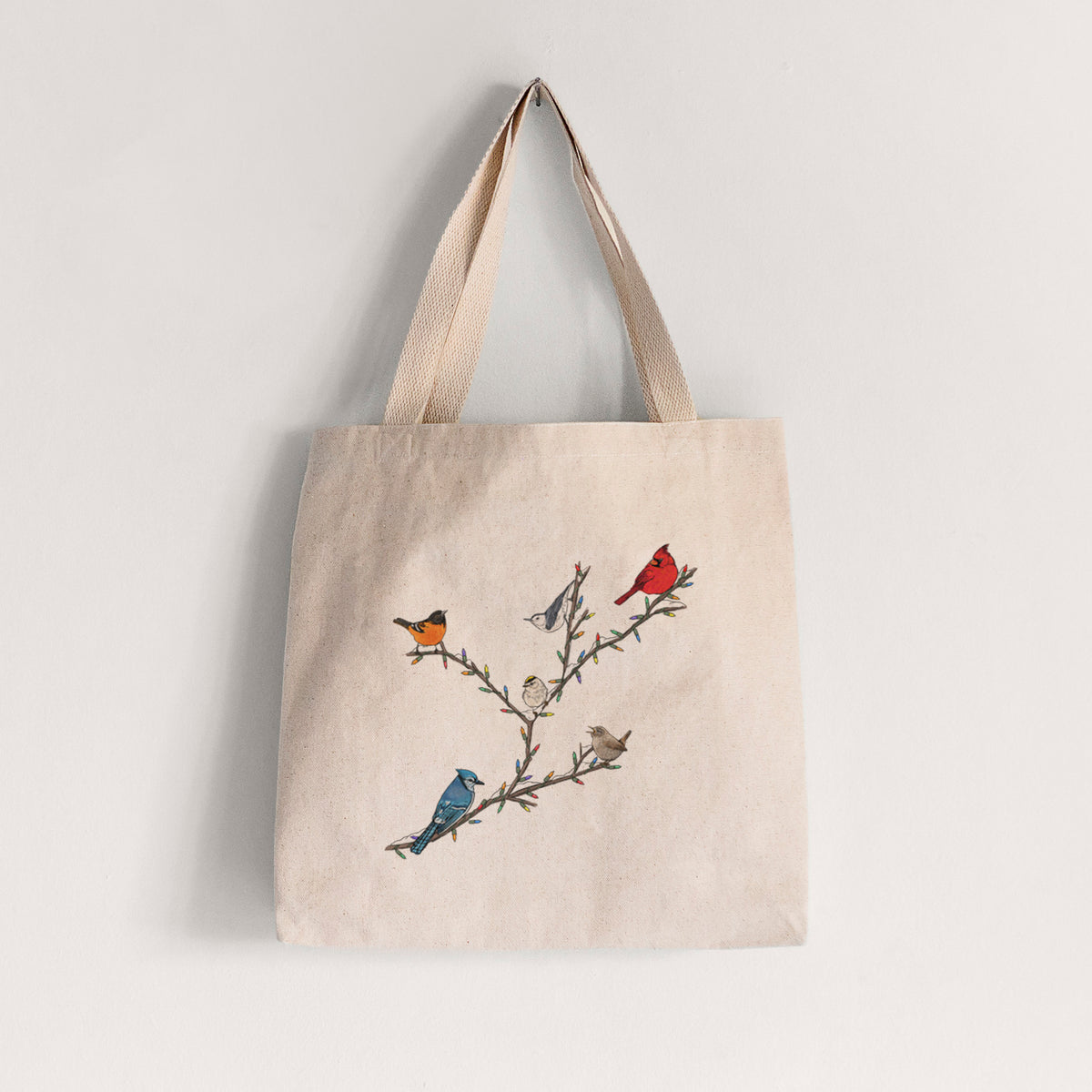 Natural canvas tote bag printed with a full-color illustration of winter backyard birds, including a cardinal, blue jay and robin, perched on bare branches.