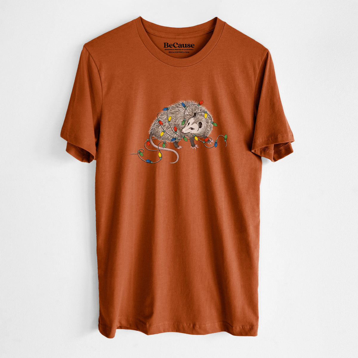 Autumn lightweight cotton t-shirt laid flat, printed with a black ink opossum tangled in a string of colorful holiday lights.