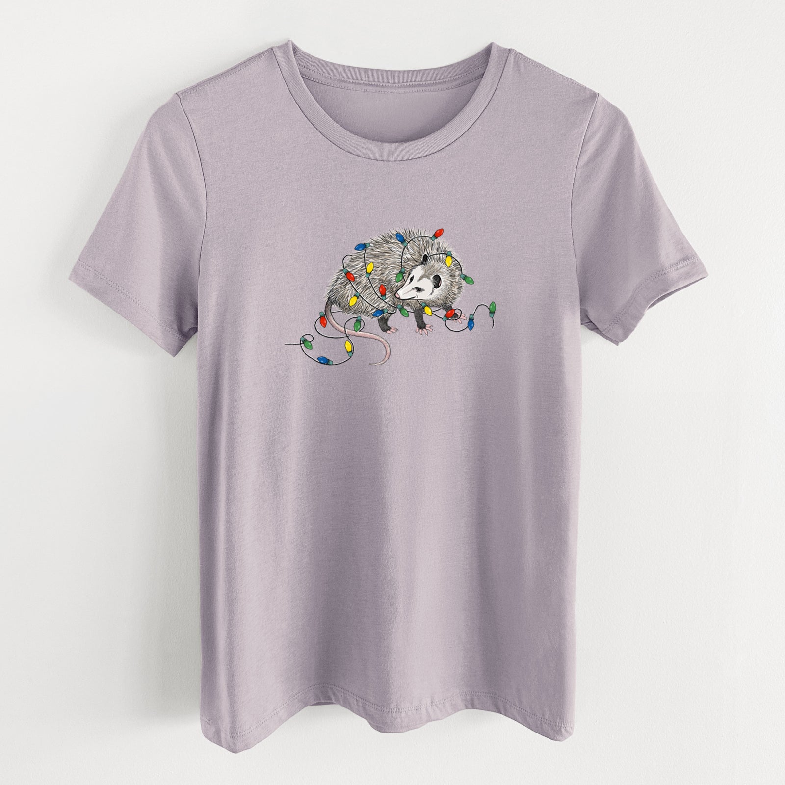 Light violet women's relaxed fit cotton t-shirt laid flat, printed with a black ink opossum tangled in a string of colorful holiday lights.