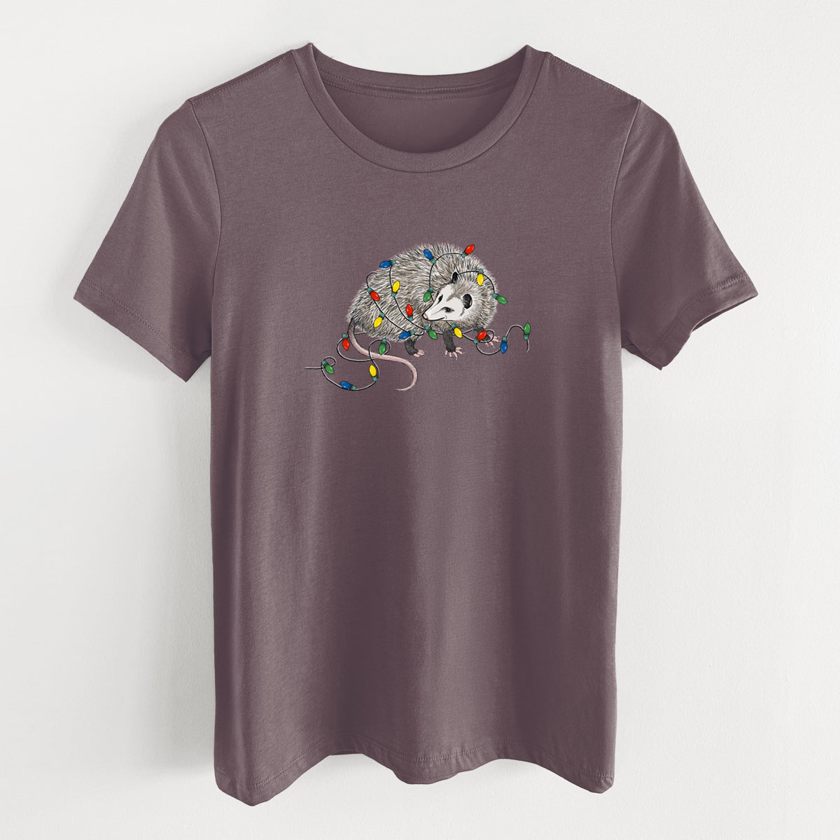 Purple storm women's relaxed fit cotton t-shirt laid flat, printed with a black ink opossum tangled in a string of colorful holiday lights.