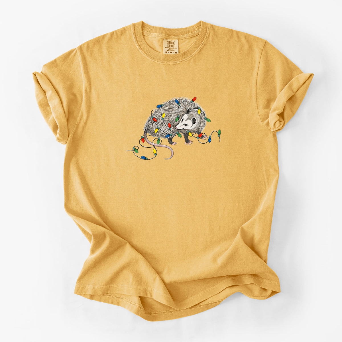 Golden wheat yellow Comfort Colors t-shirt laid flat, printed with a black ink opossum tangled in a string of colorful holiday lights.