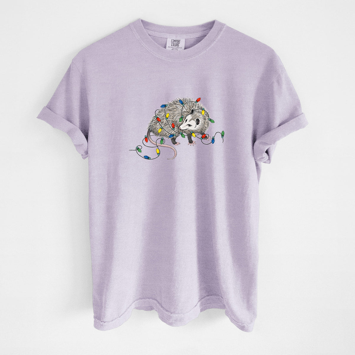 Orchid purple Comfort Colors t-shirt laid flat, printed with a black ink opossum tangled in a string of colorful holiday lights.