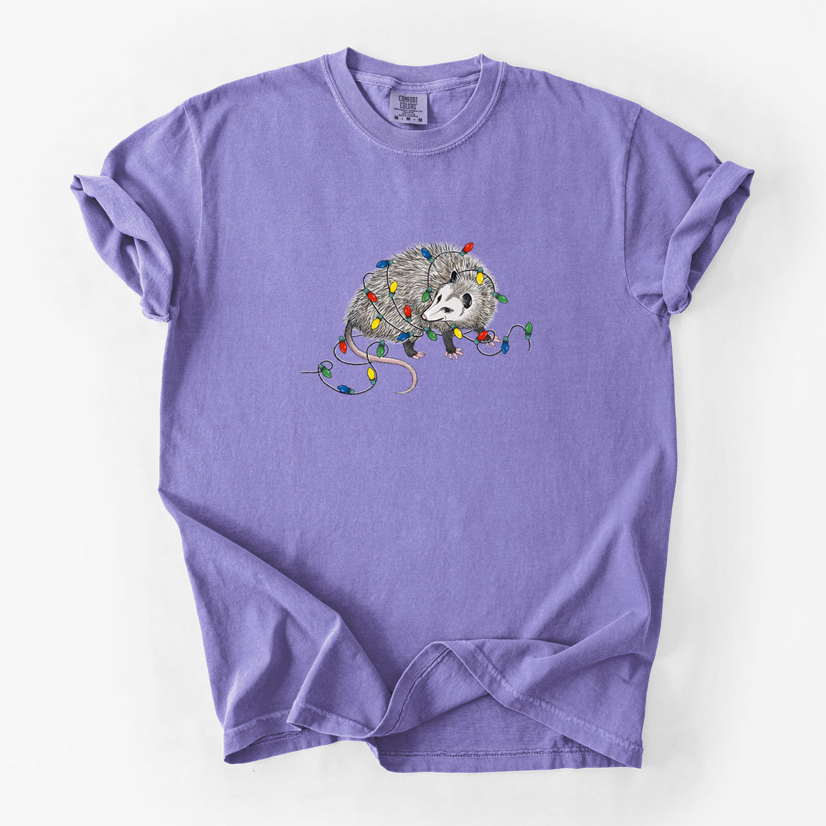 Violet purple Comfort Colors t-shirt laid flat, printed with a black ink opossum tangled in a string of colorful holiday lights.