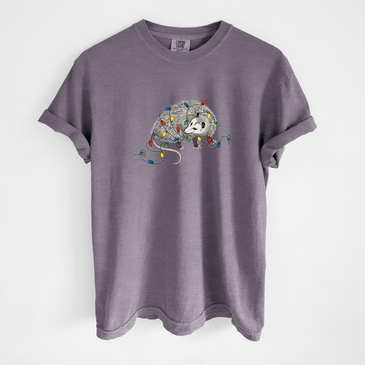 Wine red Comfort Colors t-shirt laid flat, printed with a black ink opossum tangled in a string of colorful holiday lights.