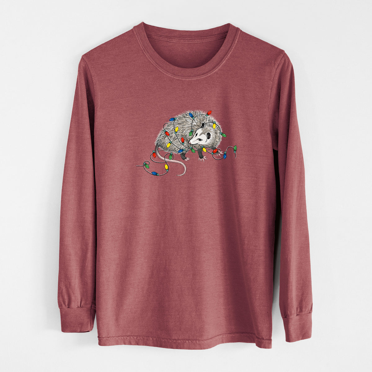 Brick red Comfort Colors long sleeve shirt laid flat, printed with a black ink opossum tangled in a string of colorful holiday lights.