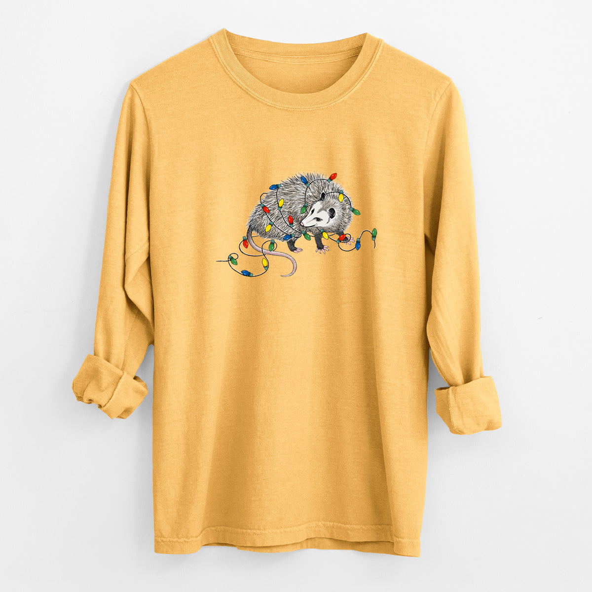 Golden wheat yellow Comfort Colors long sleeve shirt laid flat with the cuffs rolled, printed with a black ink opossum tangled in a string of colorful holiday lights.