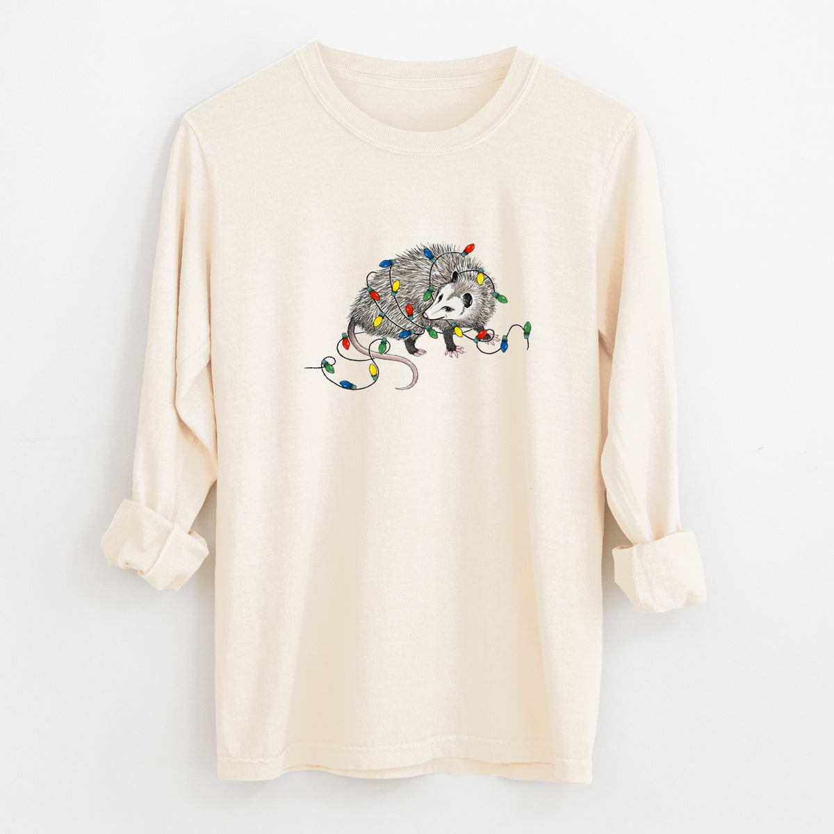 Ivory Comfort Colors long sleeve shirt laid flat with the cuffs rolled, printed with a black ink opossum tangled in a string of colorful holiday lights.