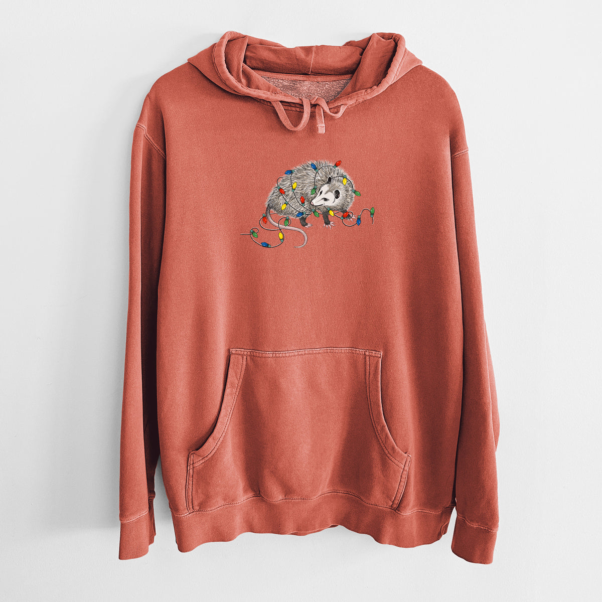 Amber orange pigment dyed hoodie laid flat, printed with a black ink opossum tangled in a string of colorful holiday lights.
