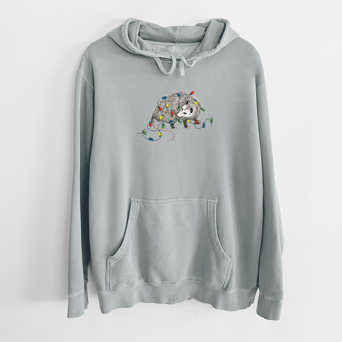 Sage green pigment dyed hoodie laid flat, printed with a black ink opossum tangled in a string of colorful holiday lights.