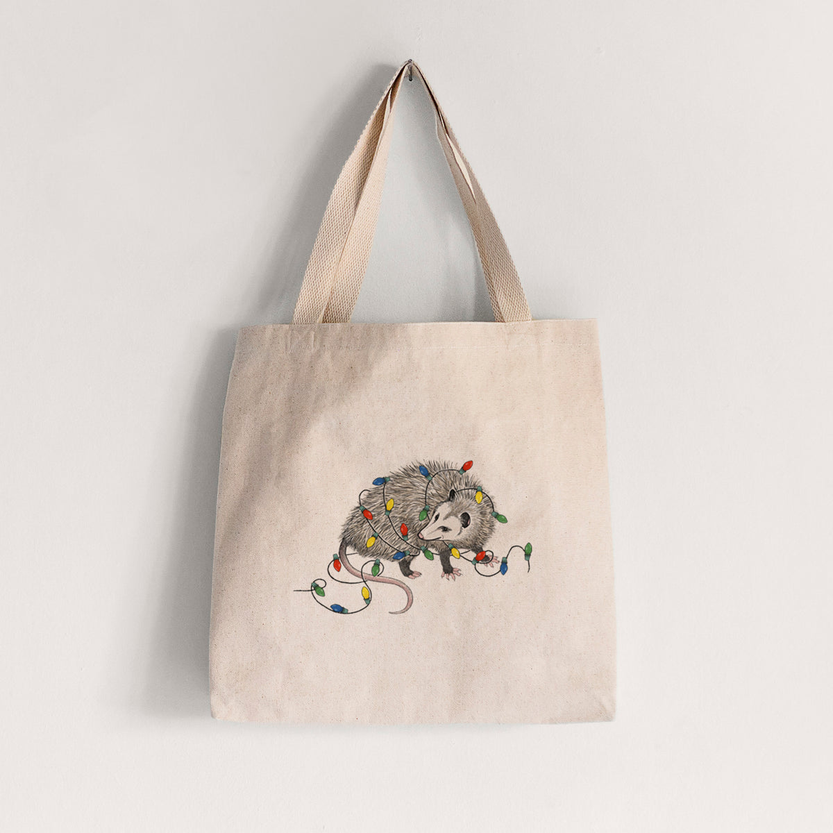 Natural canvas tote bag printed with a black ink opossum tangled in a string of colorful holiday lights.
