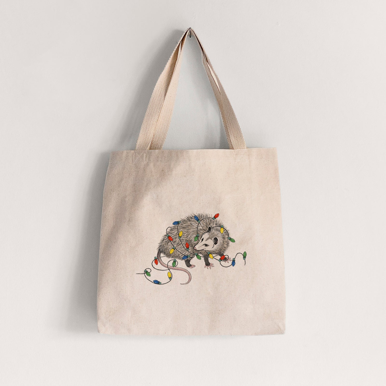 Natural canvas tote bag printed with a black ink opossum tangled in a string of colorful holiday lights.