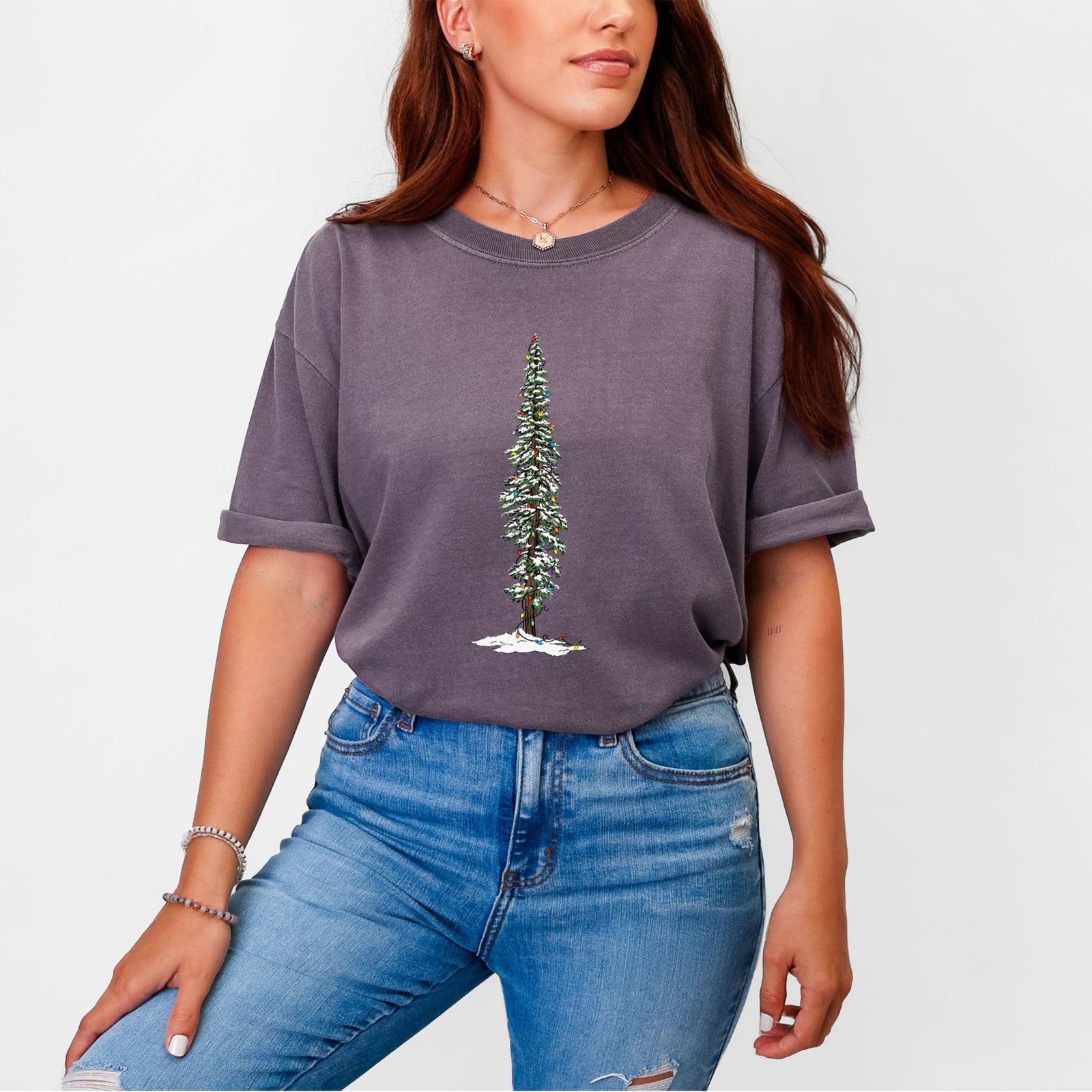 Blue jean Comfort Colors t-shirt laid flat, printed with a full-color illustration of a tall redwood tree dusted with snow and strung with holiday lights.
