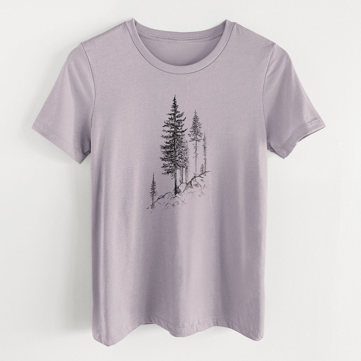 Light violet women's relaxed fit cotton t-shirt laid flat, printed with a black ink illustration of tall pine trees growing from a rocky cliff.