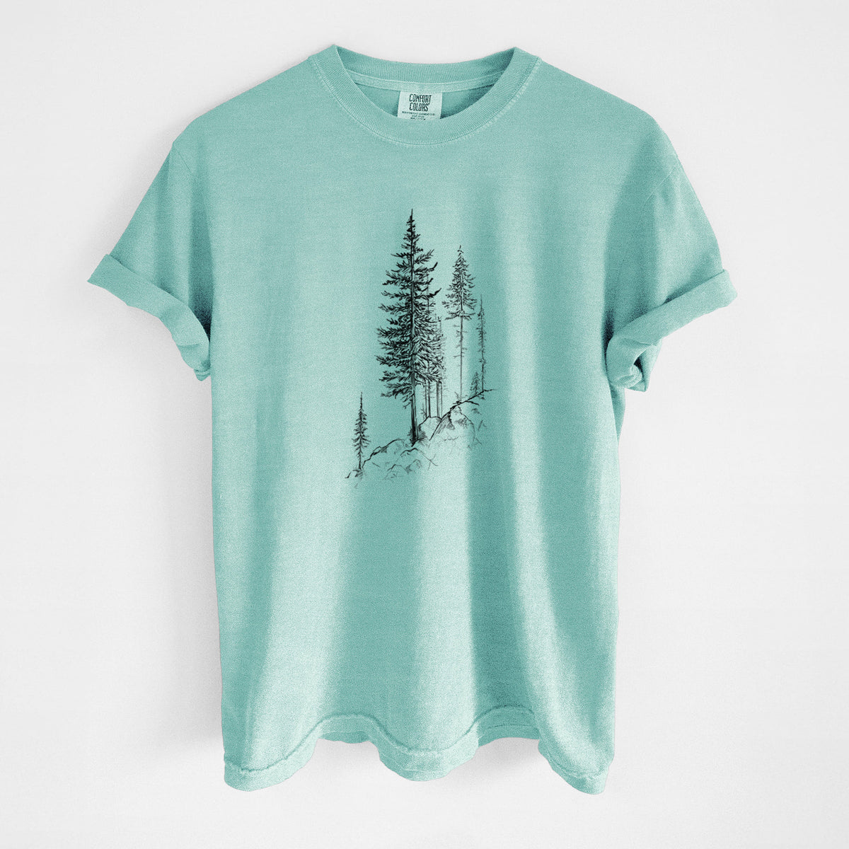 Chalky mint Comfort Colors t-shirt laid flat, printed with a black ink illustration of tall pine trees growing from a rocky cliff.
