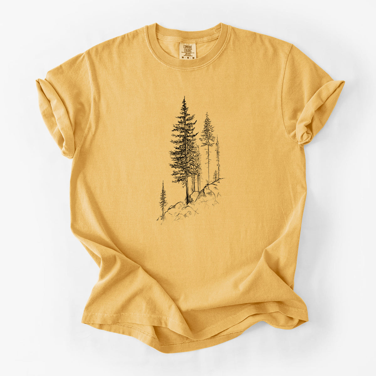 Golden wheat yellow Comfort Colors t-shirt laid flat, printed with a black ink illustration of tall pine trees growing from a rocky cliff.