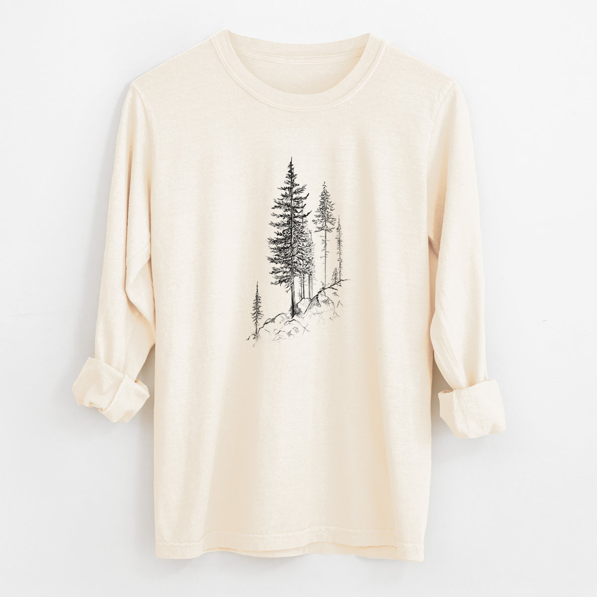 Ivory Comfort Colors long sleeve shirt laid flat with the cuffs rolled, printed with a black ink illustration of tall pine trees growing from a rocky cliff.