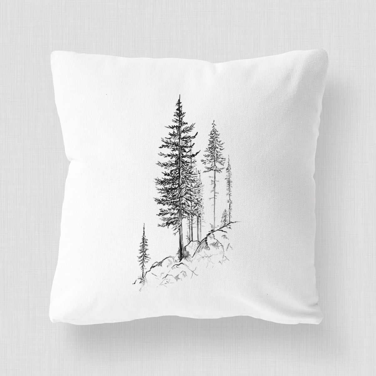 White pillow cover printed with a black ink illustration of tall pine trees growing from a rocky cliff.