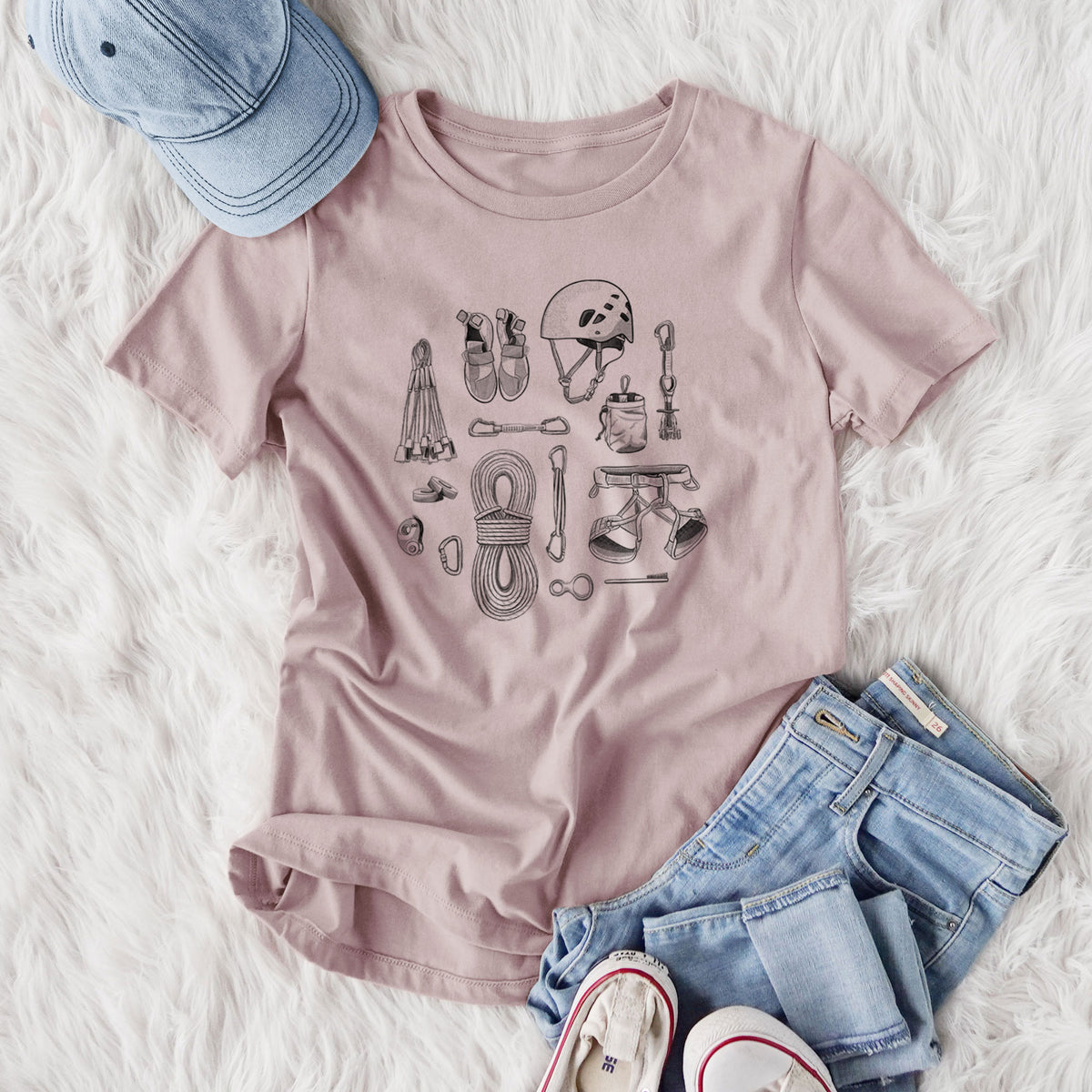 Women's relaxed fit cotton t-shirt printed with a black ink flat lay of rock climbing gear, including a helmet, shoes, rope, harness and carabiners, styled flat on a white faux fur rug with jeans.