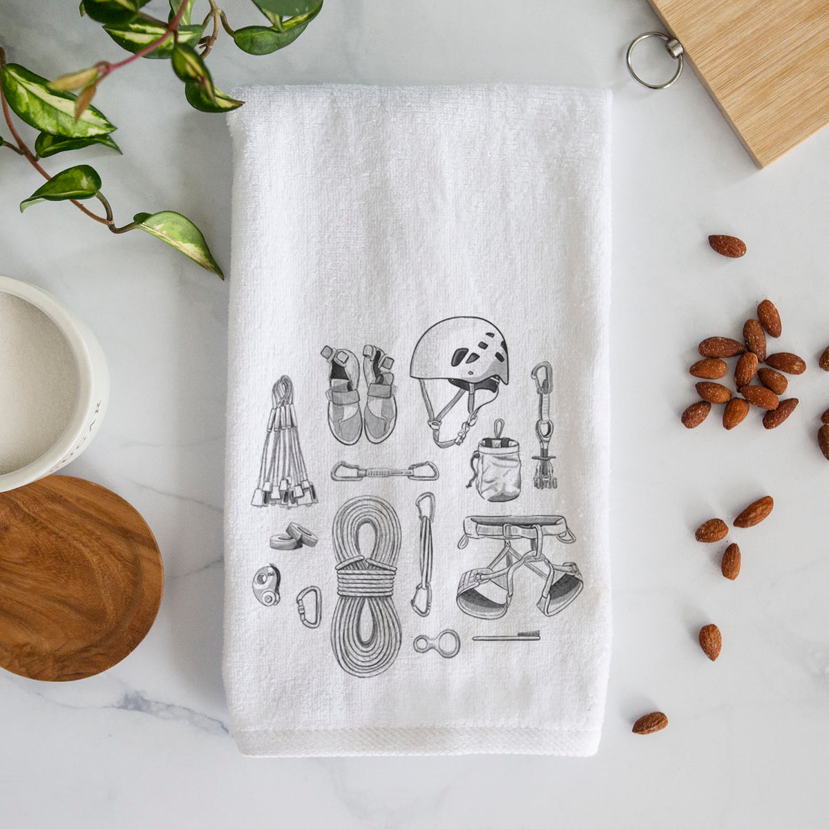 White hand towel printed with a black ink flat lay of rock climbing gear, including a helmet, shoes, rope, harness and carabiners.