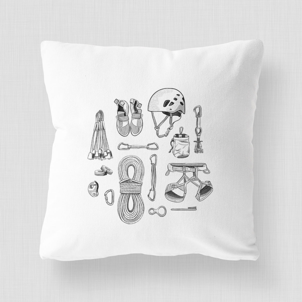 White pillow cover printed with a black ink flat lay of rock climbing gear, including a helmet, shoes, rope, harness and carabiners.