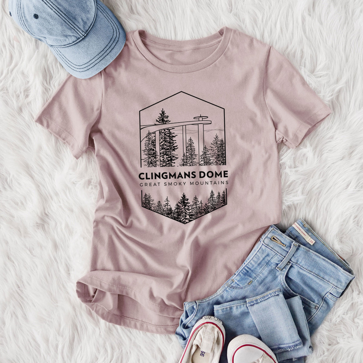 Women's relaxed fit cotton t-shirt printed with a black line art badge of the Clingmans Dome observation tower above a pine forest, with the words Clingmans Dome, Great Smoky Mountains, styled flat on a white faux fur rug with jeans.