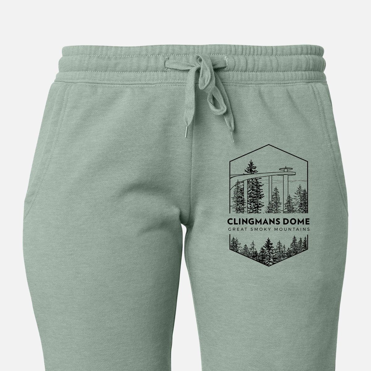 Front of sage green Cali Wave sweatpants, printed with a black line art badge of the Clingmans Dome observation tower above a pine forest, with the words Clingmans Dome, Great Smoky Mountains on the leg.