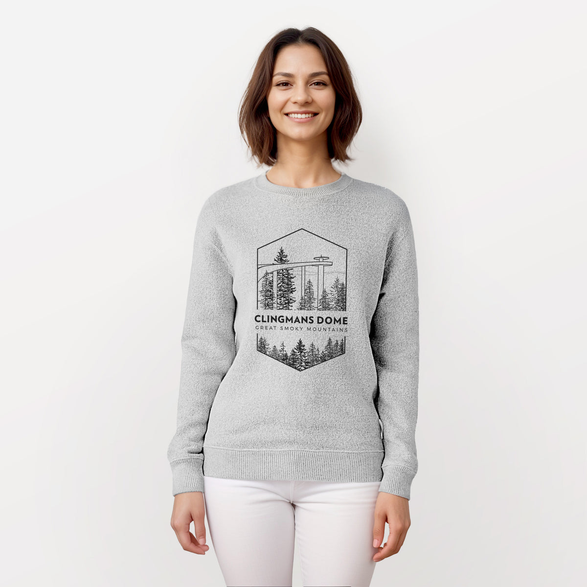 Woman wearing a knit sweatshirt printed with a black line art badge of the Clingmans Dome observation tower above a pine forest, with the words Clingmans Dome, Great Smoky Mountains.