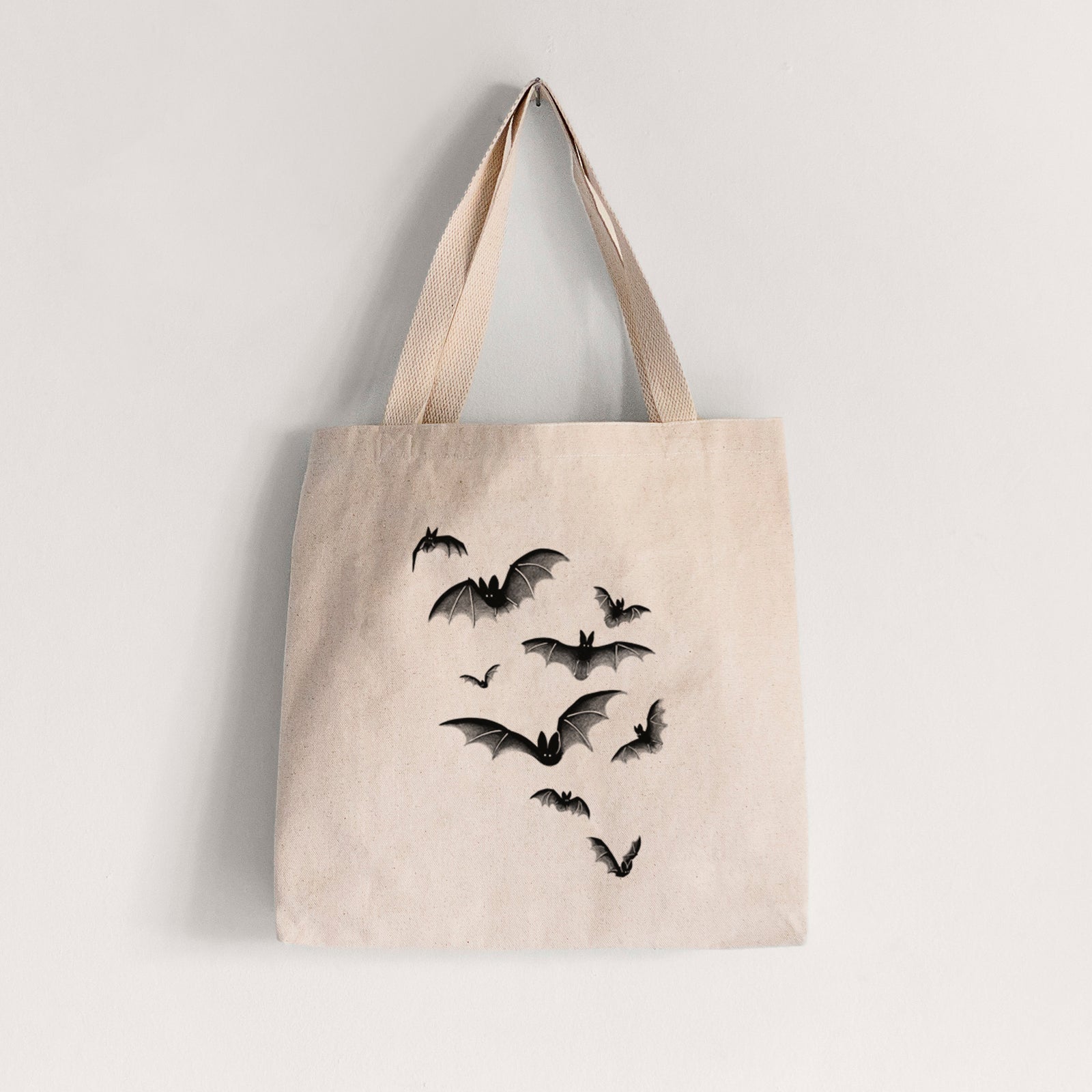Natural canvas tote bag printed with a black ink illustration of a cloud of bats in flight.