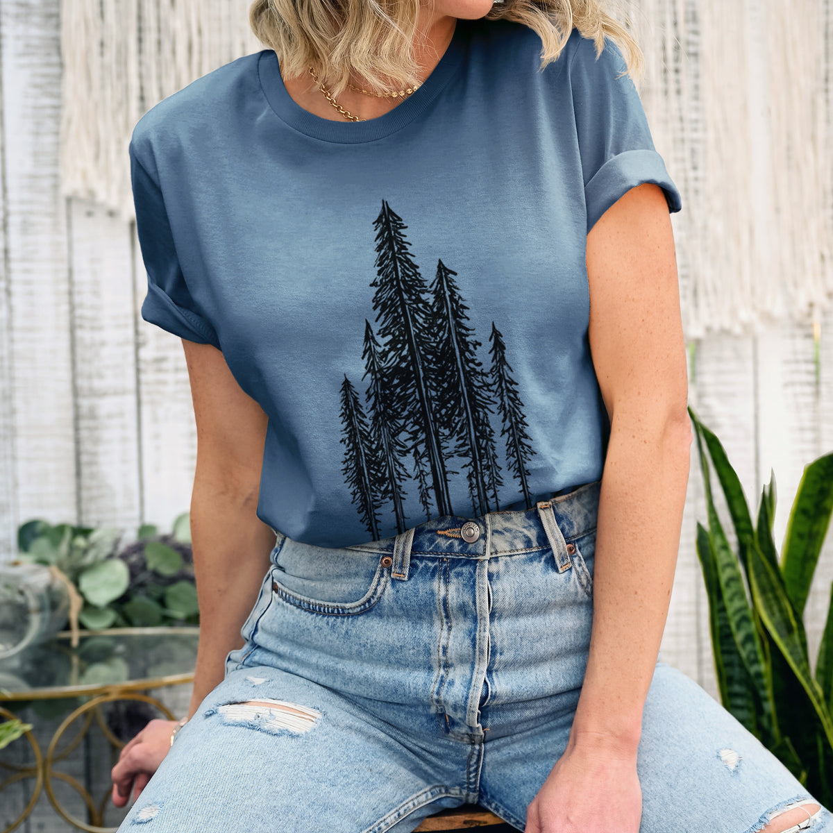 Woman wearing a steel blue lightweight cotton t-shirt printed with a black ink illustration of a stand of tall coastal redwood trees with slender trunks and layered branches.
