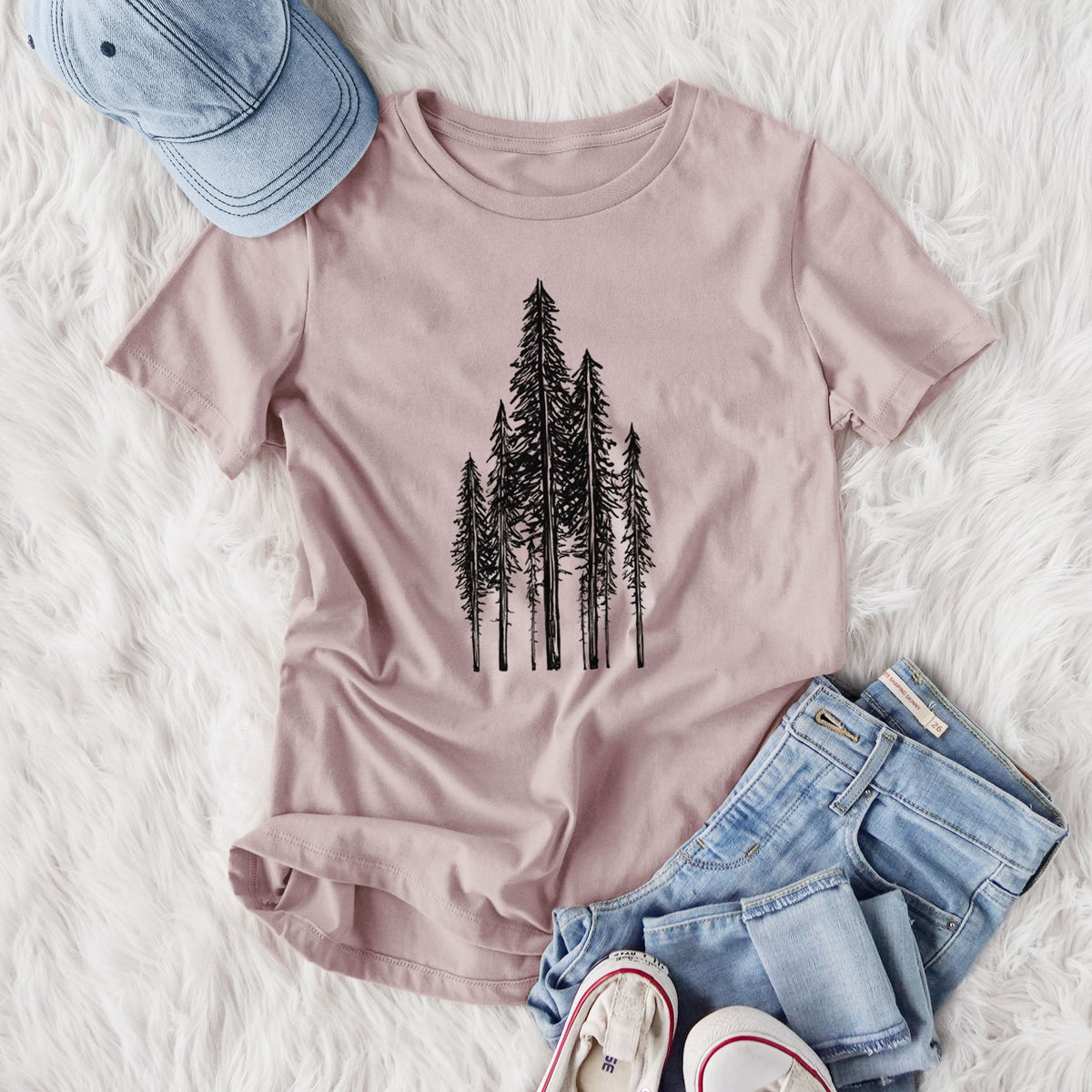 Women's relaxed fit cotton t-shirt printed with a black ink illustration of a stand of tall coastal redwood trees with slender trunks and layered branches, styled flat on a white faux fur rug with jeans.