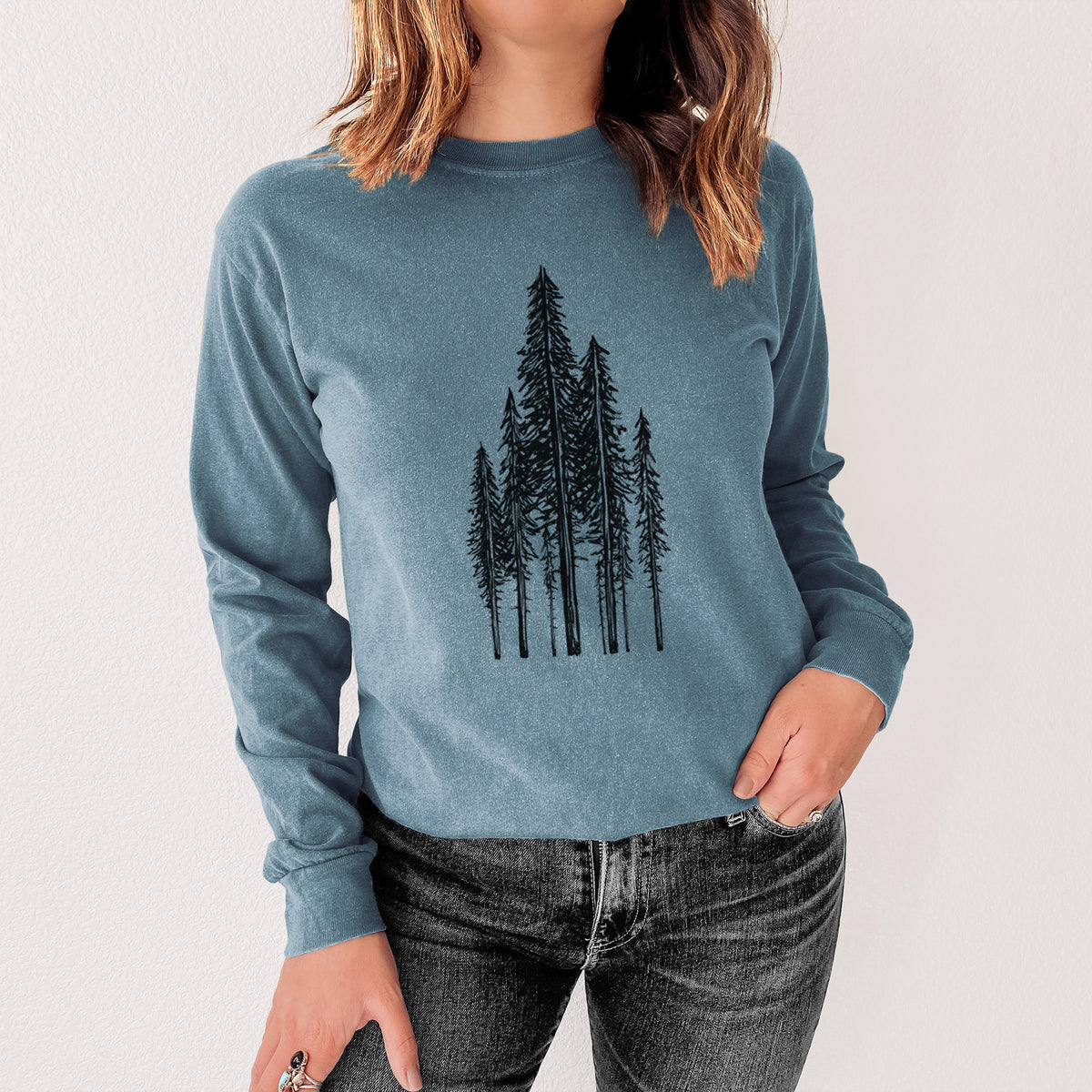 Steel blue Comfort Colors long sleeve shirt printed with a black ink illustration of a stand of tall coastal redwood trees with slender trunks and layered branches, shown in a lifestyle photo.