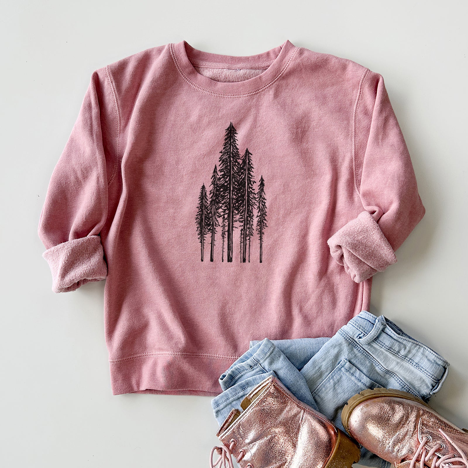 Boy wearing a youth crewneck sweatshirt printed with a black ink illustration of a stand of tall coastal redwood trees with slender trunks and layered branches, outdoors.