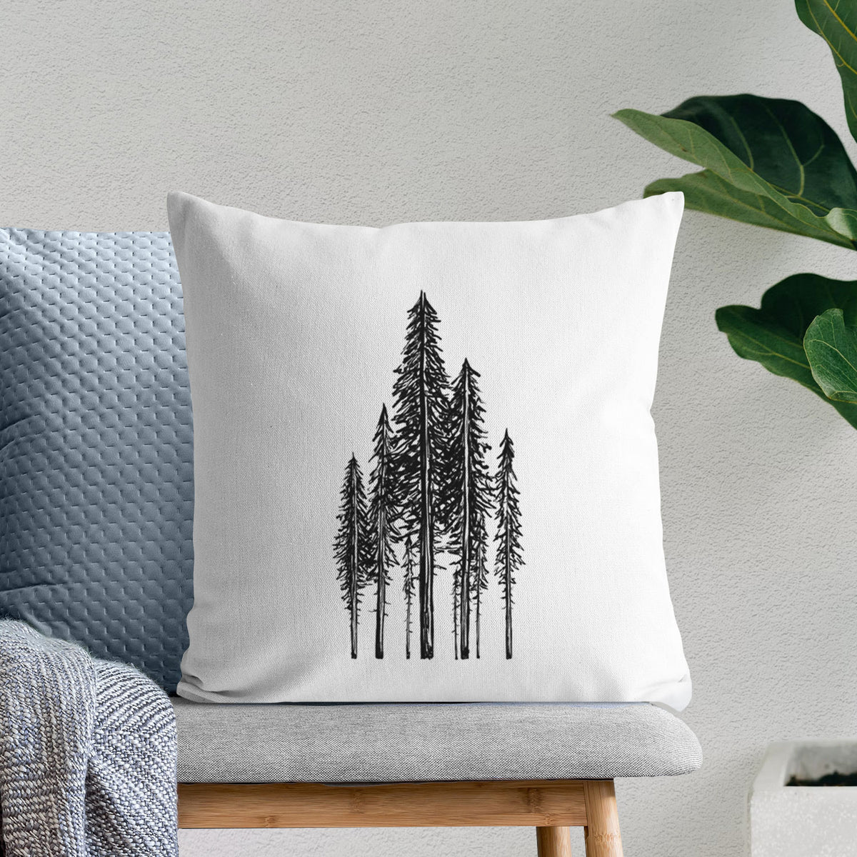 White pillow cover printed with a black ink illustration of a stand of tall coastal redwood trees with slender trunks and layered branches, on a bench beside plants.