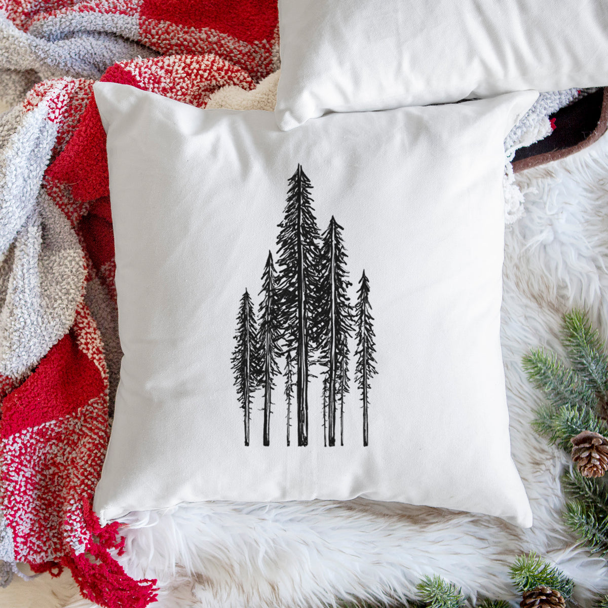 White pillow cover printed with a black ink illustration of a stand of tall coastal redwood trees with slender trunks and layered branches, on a woven chair.